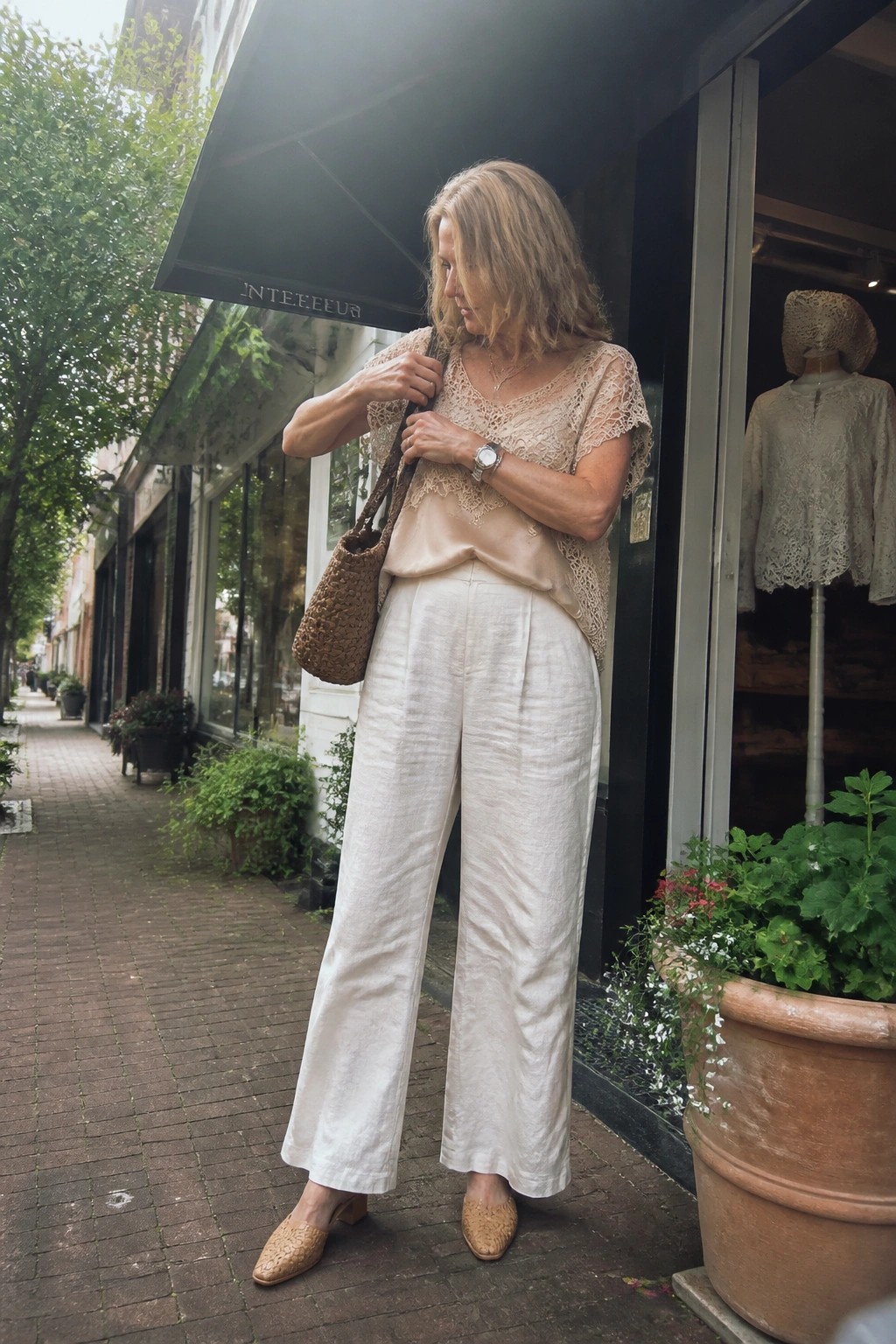 Woman in lace top and white linen pants with woven bag on sidewalk