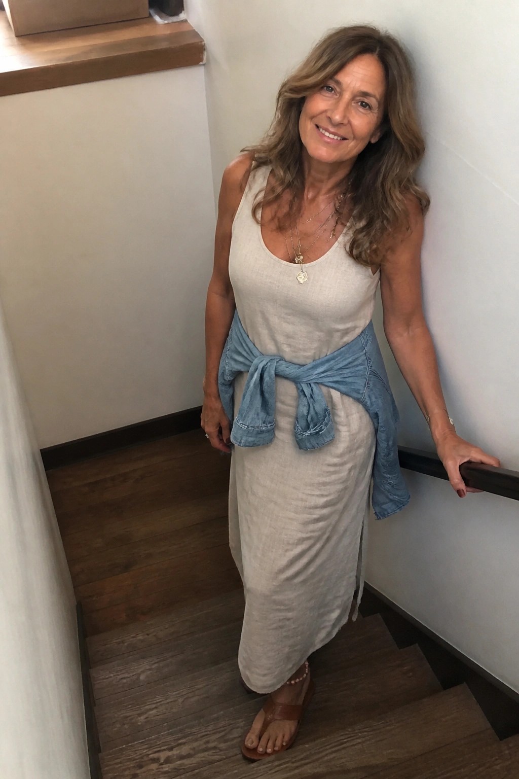 Woman in beige linen dress with denim shirt tied at waist on stairs