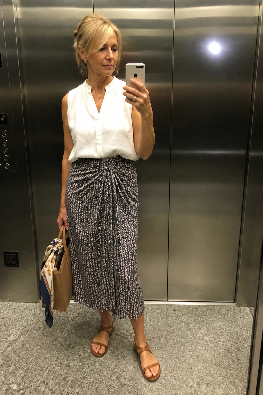 Woman in white sleeveless top and patterned skirt taking elevator selfie