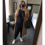 Woman in blue top and tan cardigan taking mirror selfie in hotel room