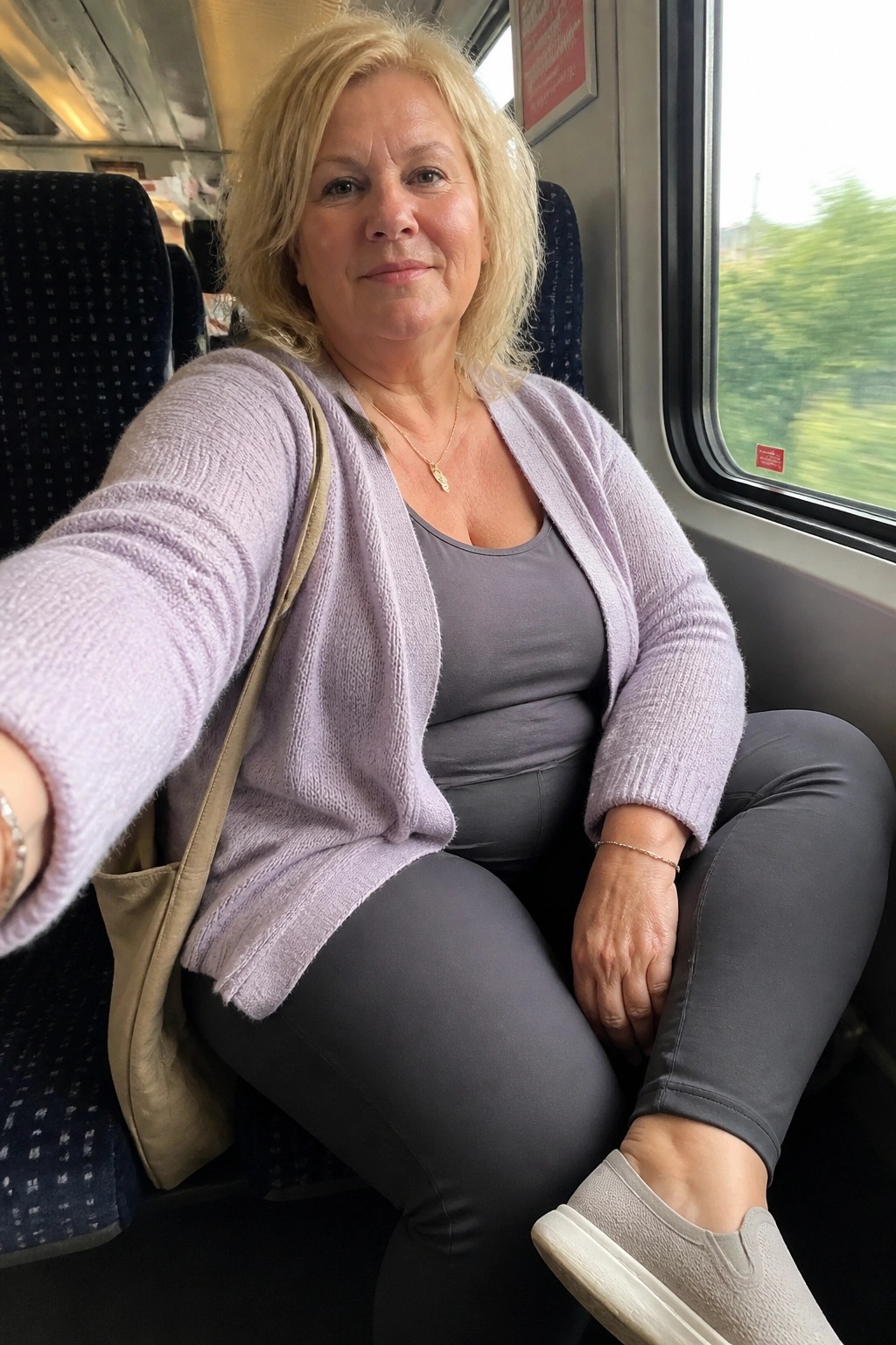 Blonde woman in light purple cardigan taking selfie on moving train by window