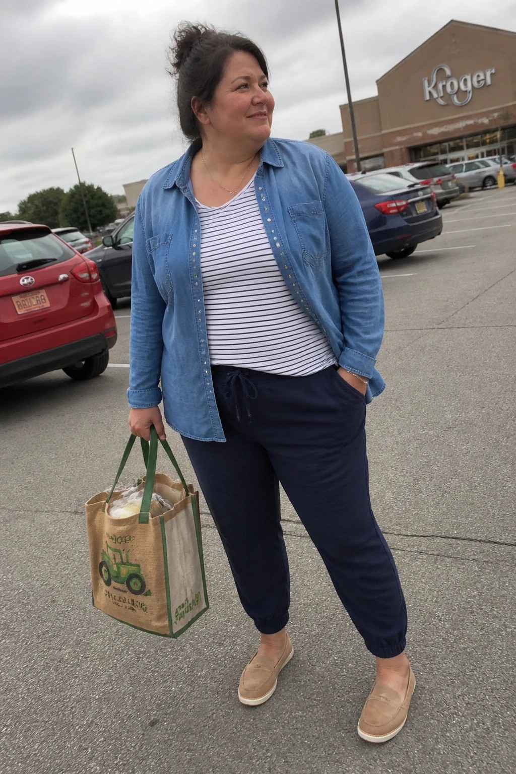 Woman in blue denim jacket holds Kroger tote bag in store parking lot