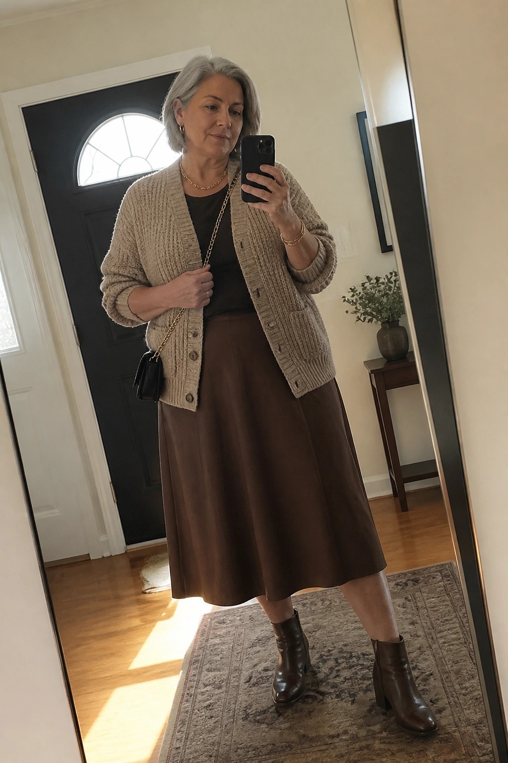 Woman with gray hair in beige cardigan and brown skirt taking mirror selfie