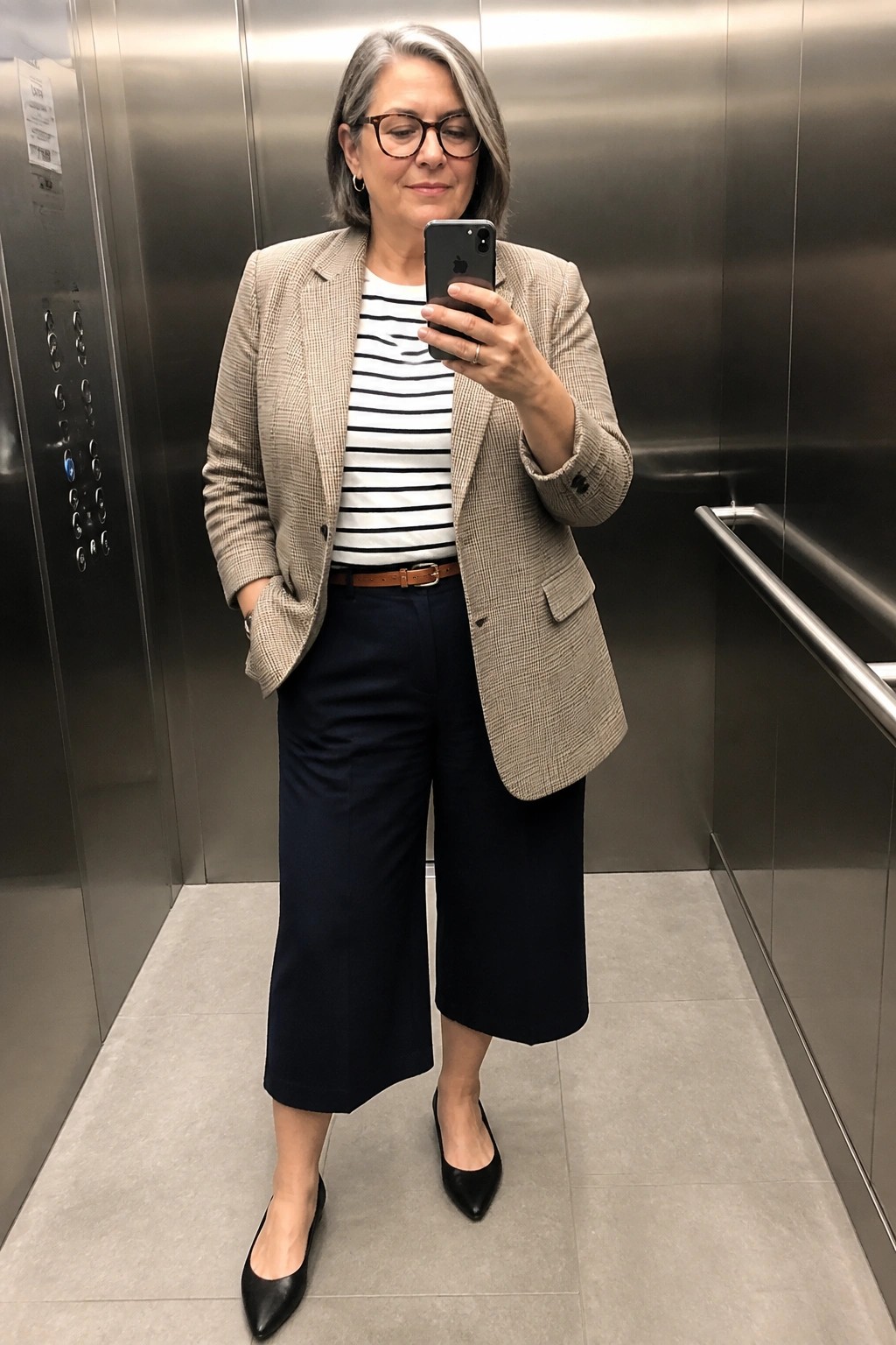 Woman in plaid blazer and striped shirt taking selfie in elevator.