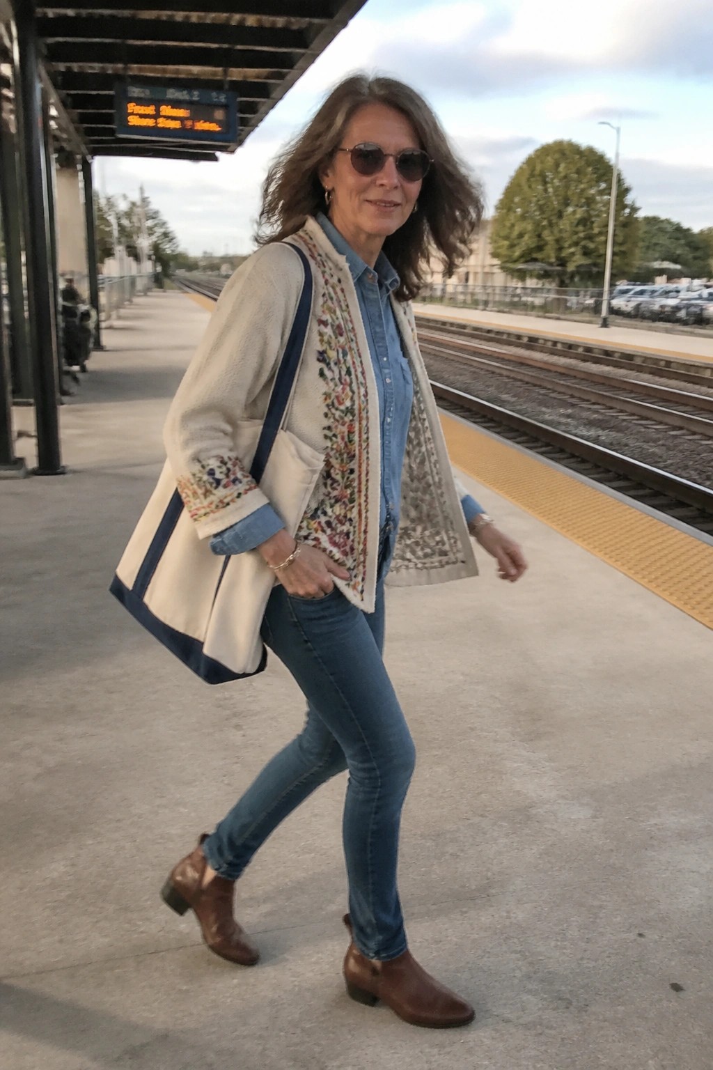 Woman in embroidered cream vest and jeans with tote bag on train platform