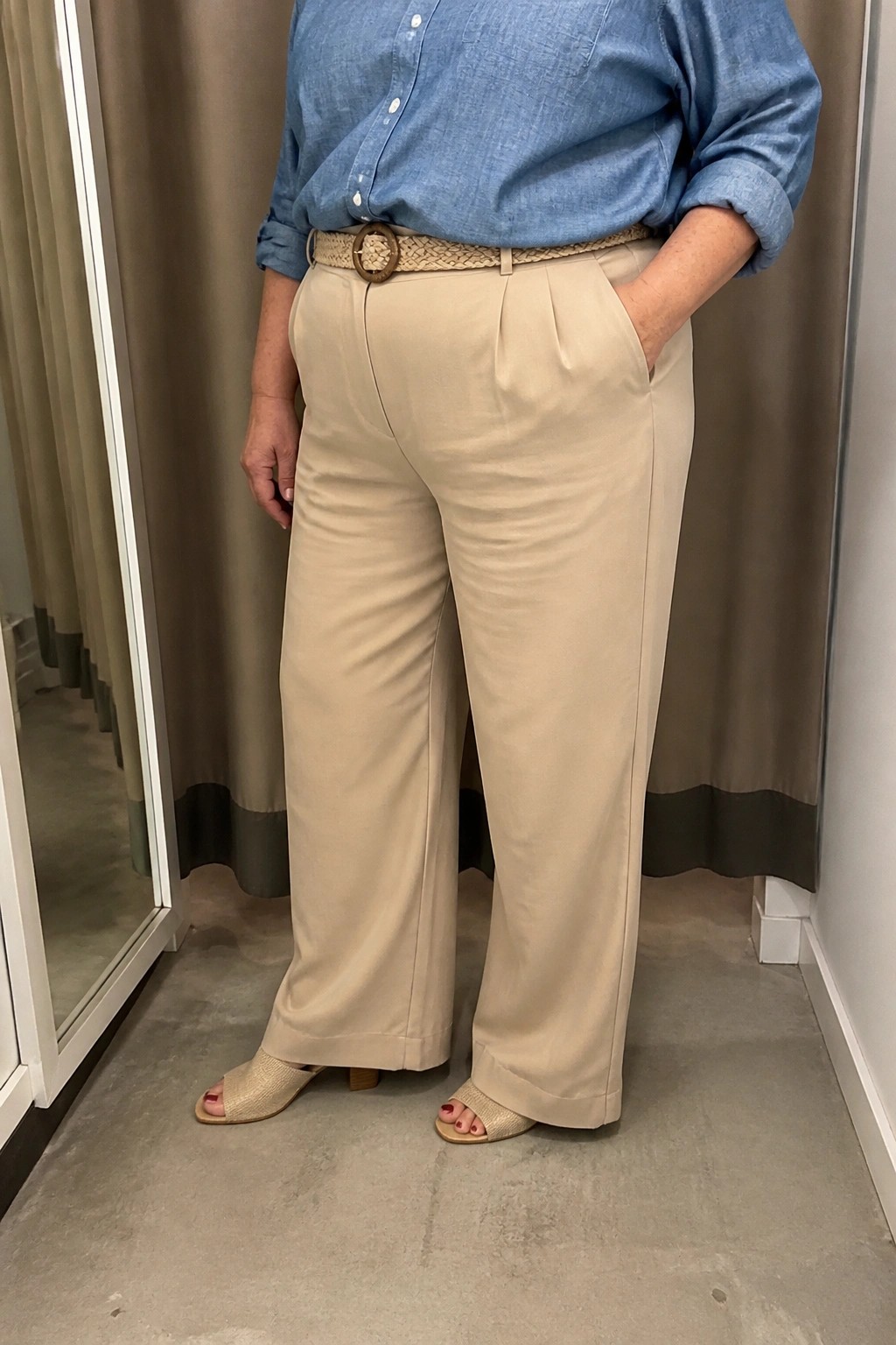 Person in beige pleated wide-leg pants, blue shirt, woven belt, and beige slides.