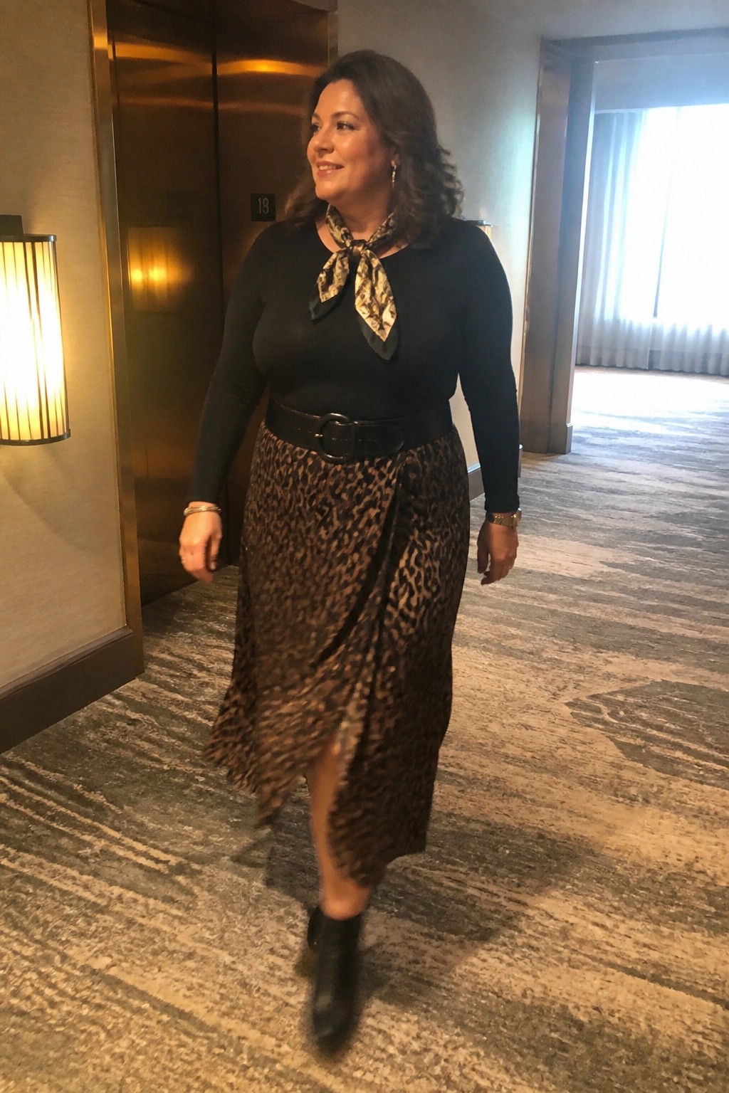 Woman in black top and leopard-print skirt walking in hotel hallway