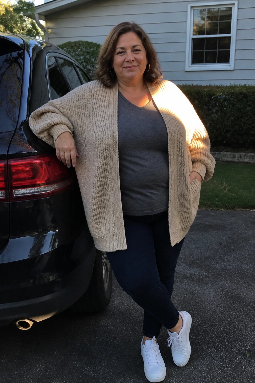 Woman in beige cardigan and jeans leaning against black SUV in driveway