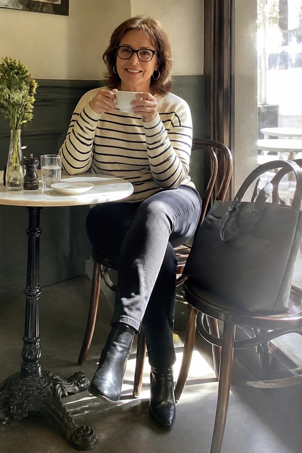 Woman in striped sweater holds white cup at marble cafe table with handbag nearby