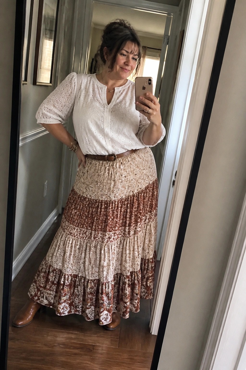 Woman in white eyelet top and tiered floral skirt taking mirror selfie with phone