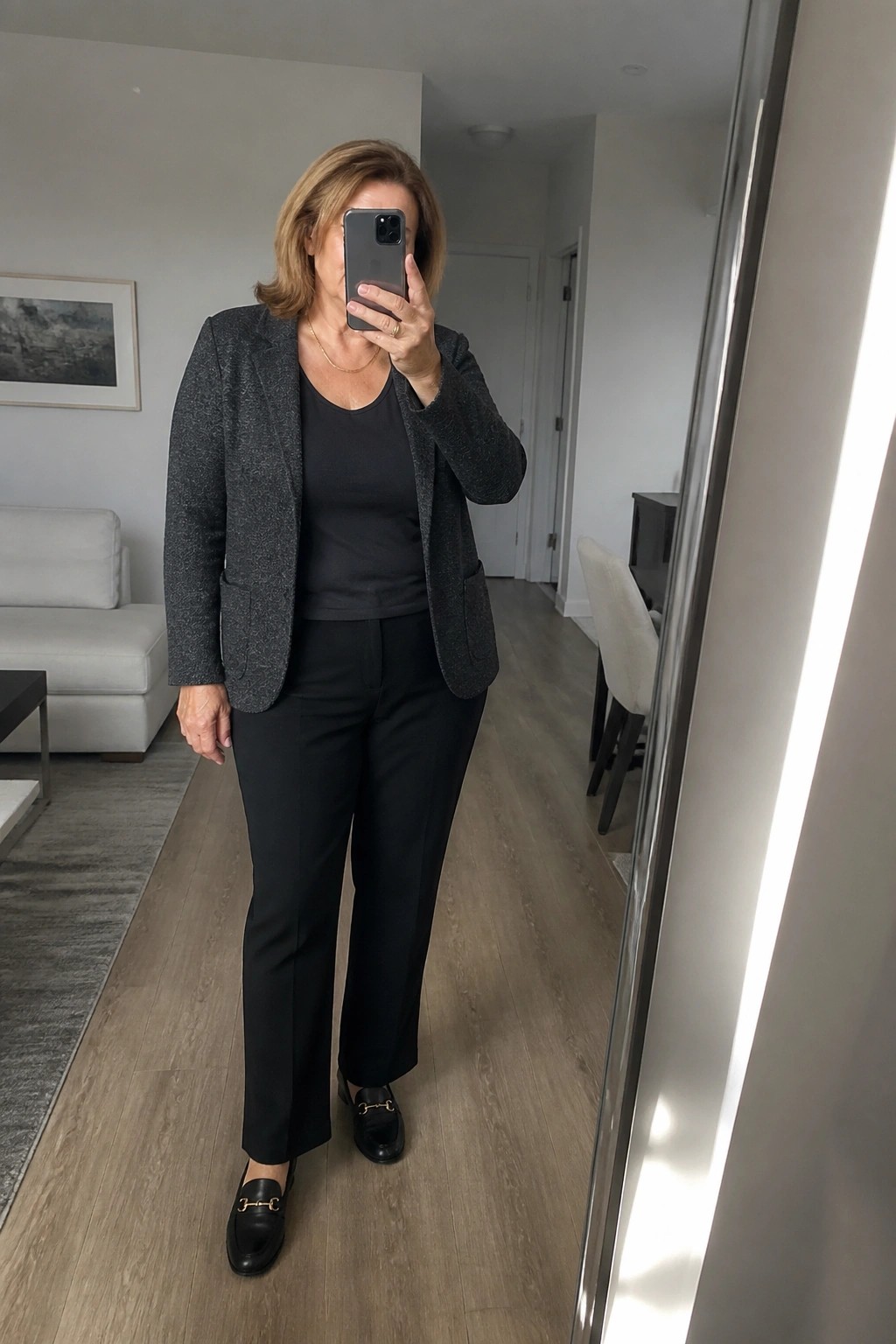 Woman in gray blazer and black pants taking mirror selfie with smartphone