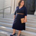 Woman in navy blue wrap dress holding clutch on stone steps