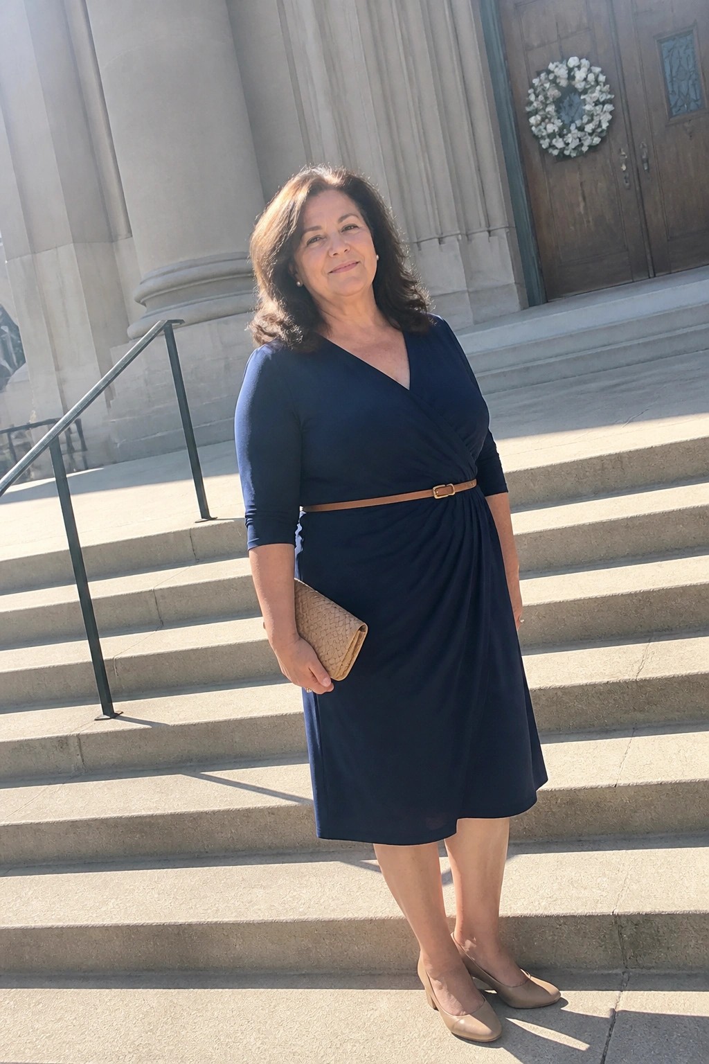 Woman in navy blue wrap dress holding clutch on stone steps