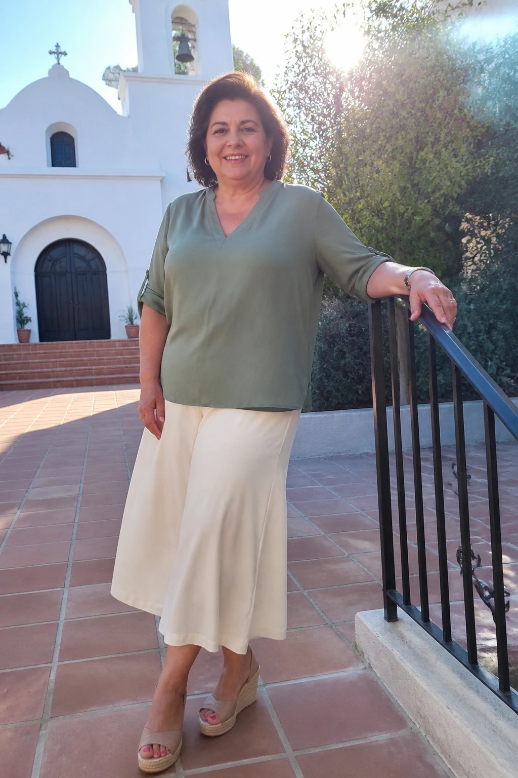 Woman in green blouse and cream skirt leaning on railing outside church
