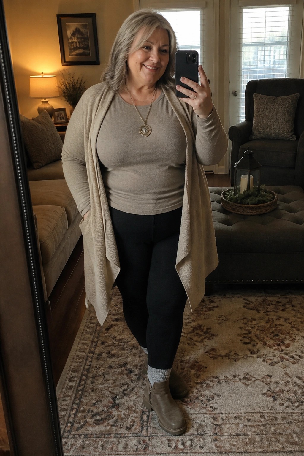 Smiling gray-haired woman in beige cardigan and black leggings taking a mirror selfie