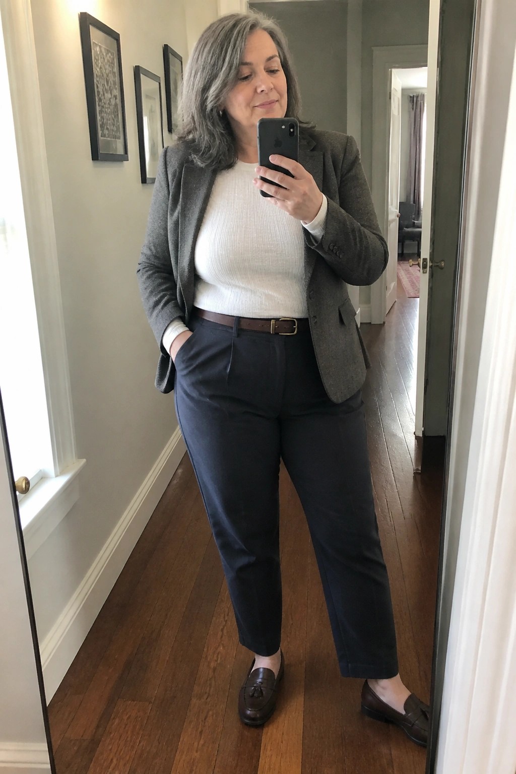 Woman with gray hair in gray blazer and navy pants taking mirror selfie
