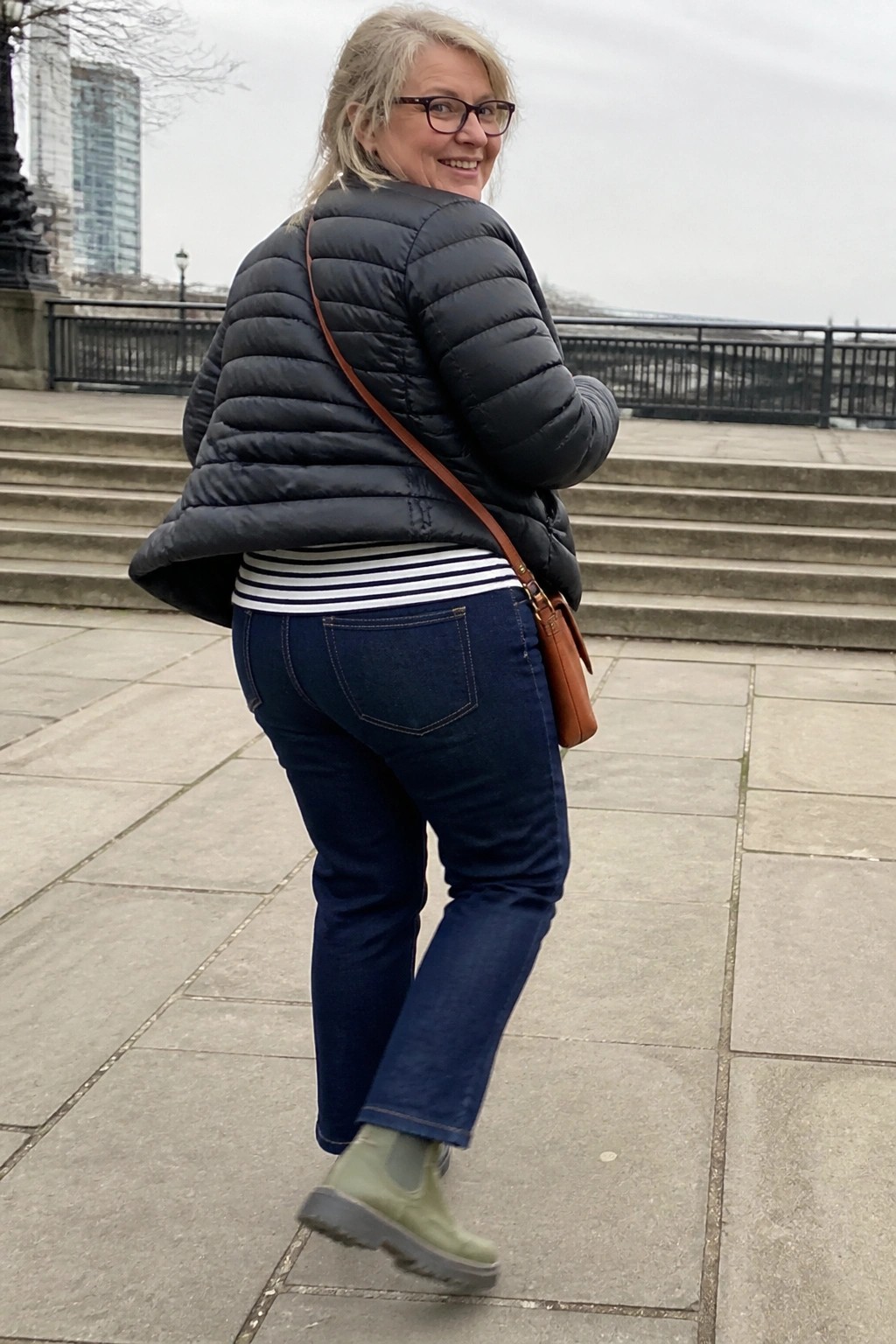 Woman in black puffer jacket and jeans with brown bag on stone steps
