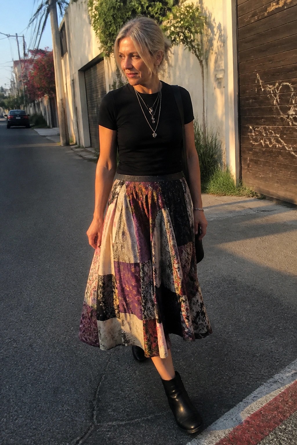 Gray-haired woman in black top and colorful patchwork skirt on urban street.