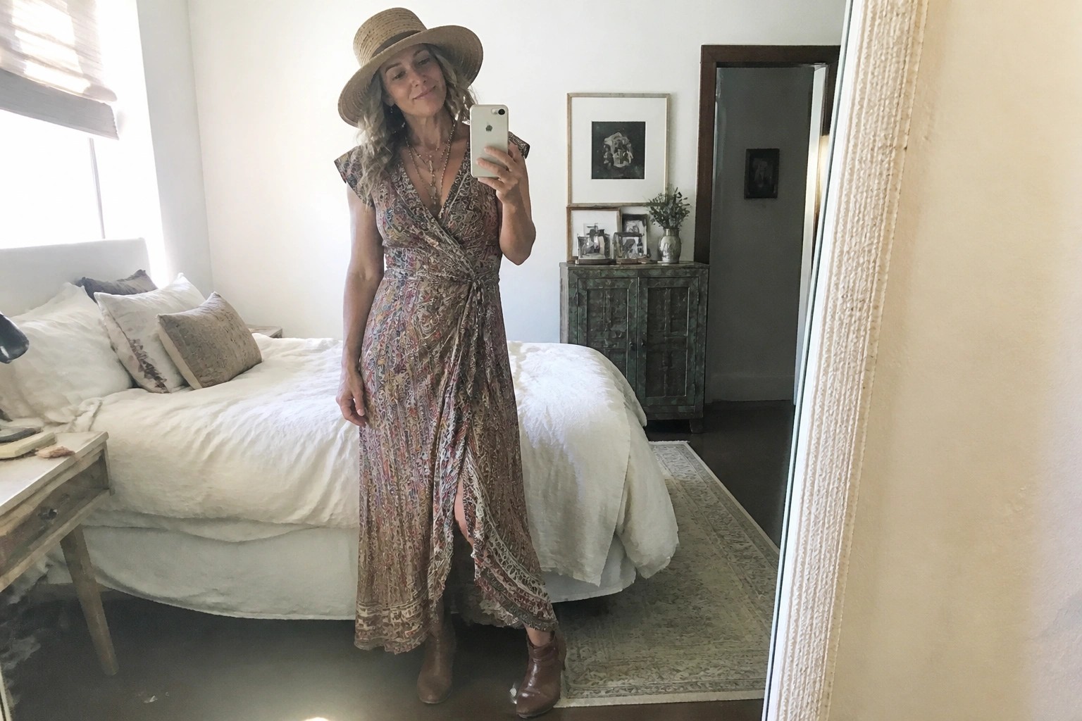 Woman in bohemian floral wrap dress, straw hat, and boots taking mirror selfie