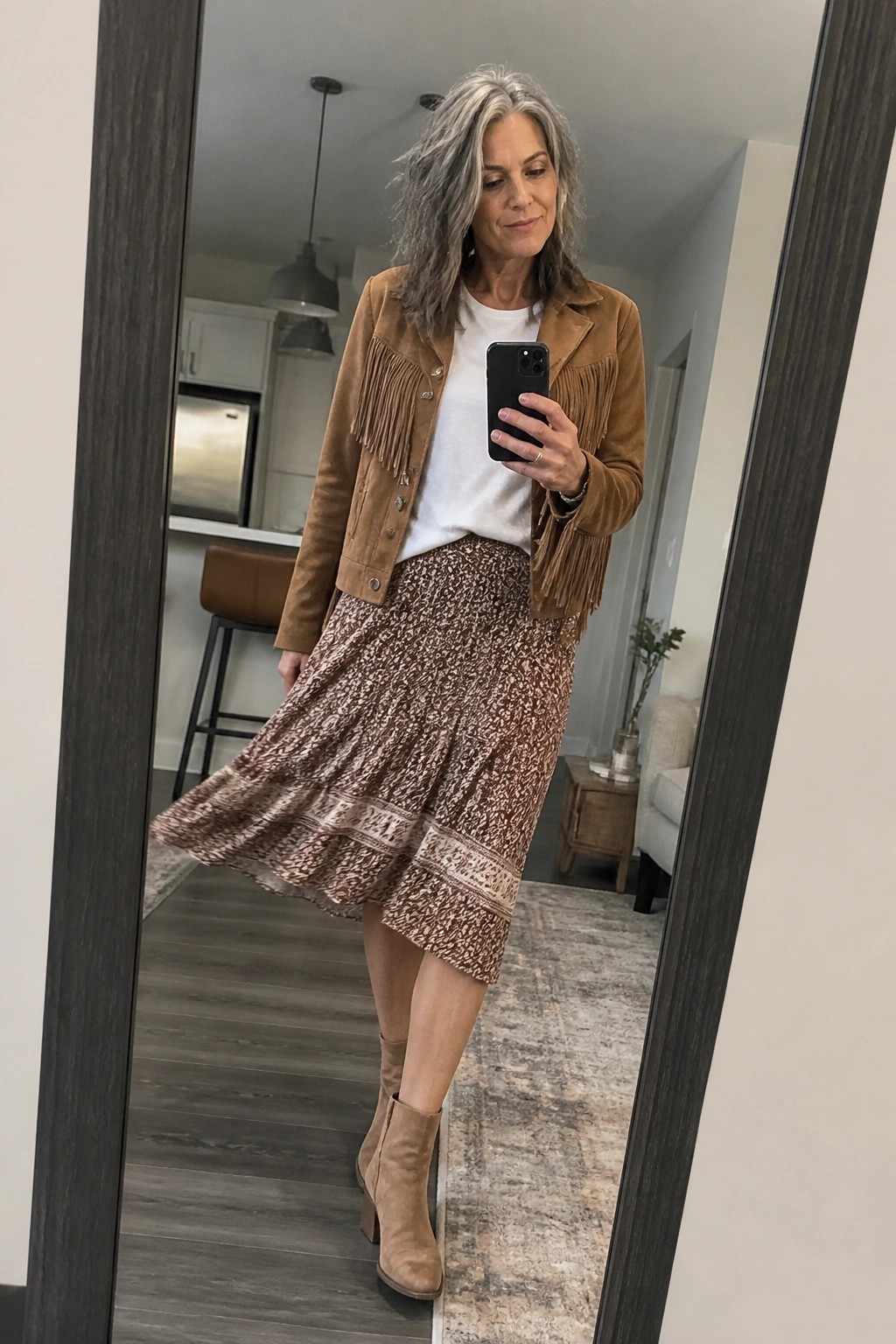 Woman with gray hair in fringed suede jacket and patterned skirt taking mirror selfie