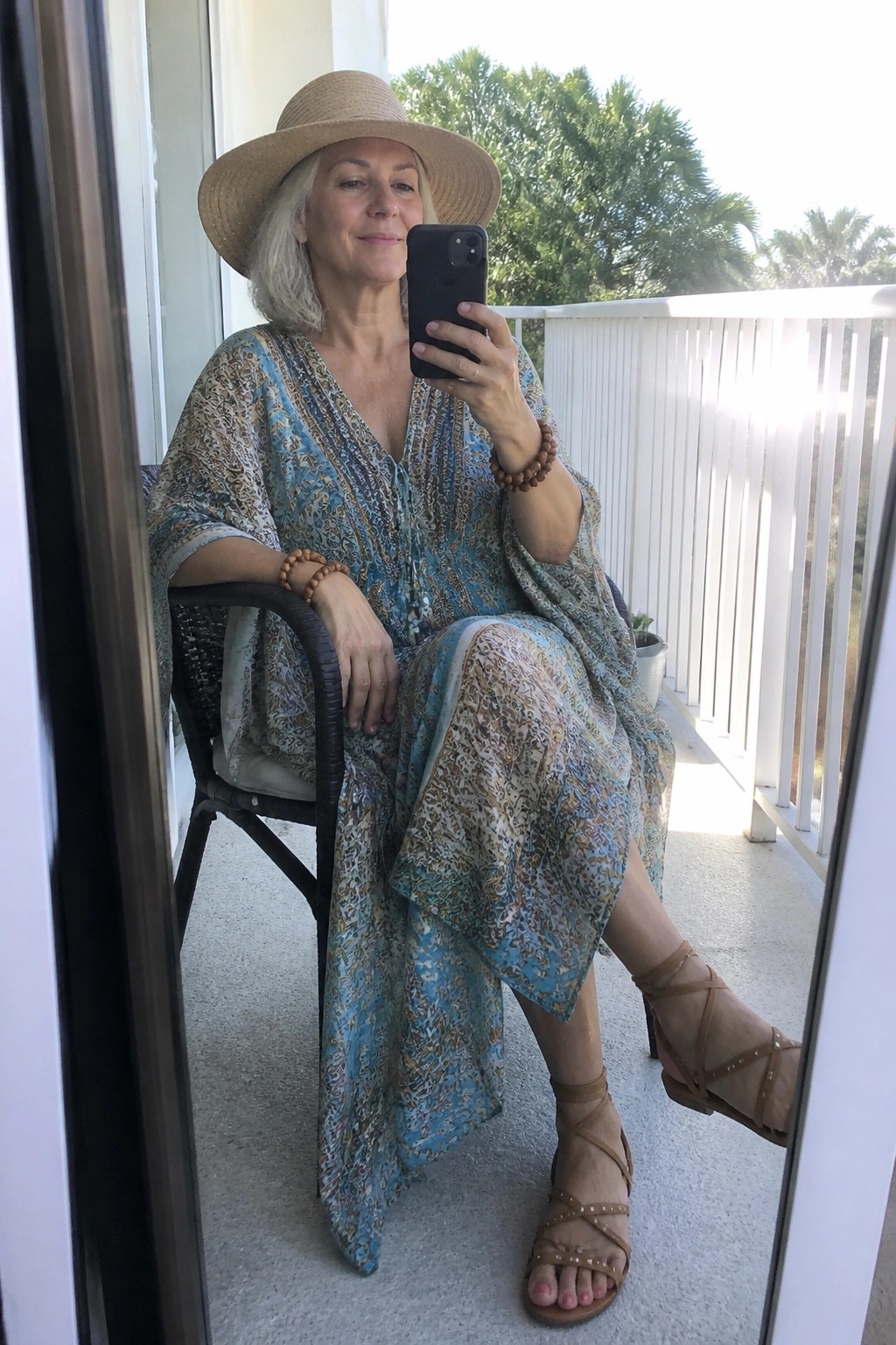 Woman in blue patterned dress and straw hat taking balcony selfie