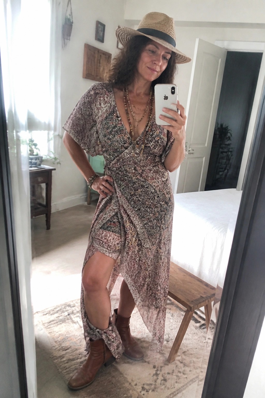 Woman in bohemian floral wrap dress, straw hat, and boots taking mirror selfie