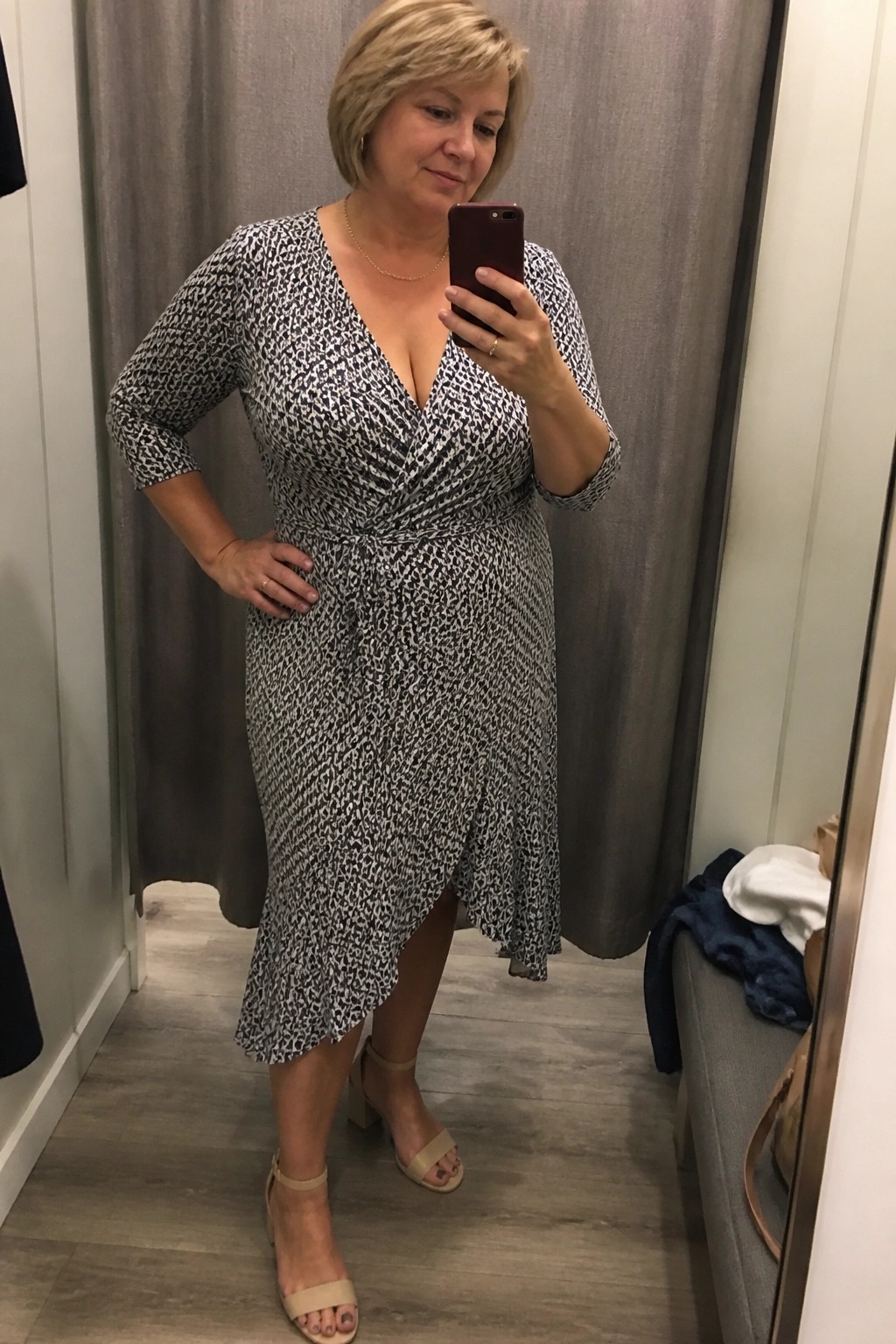 Woman in black-and-white patterned wrap dress taking mirror selfie in fitting room