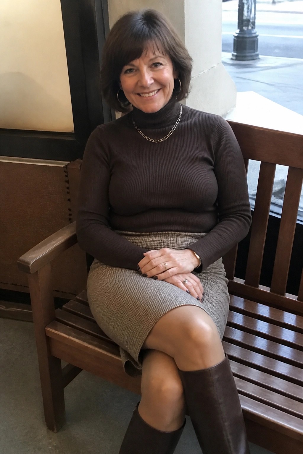 Smiling woman in brown turtleneck and patterned skirt seated on wooden bench