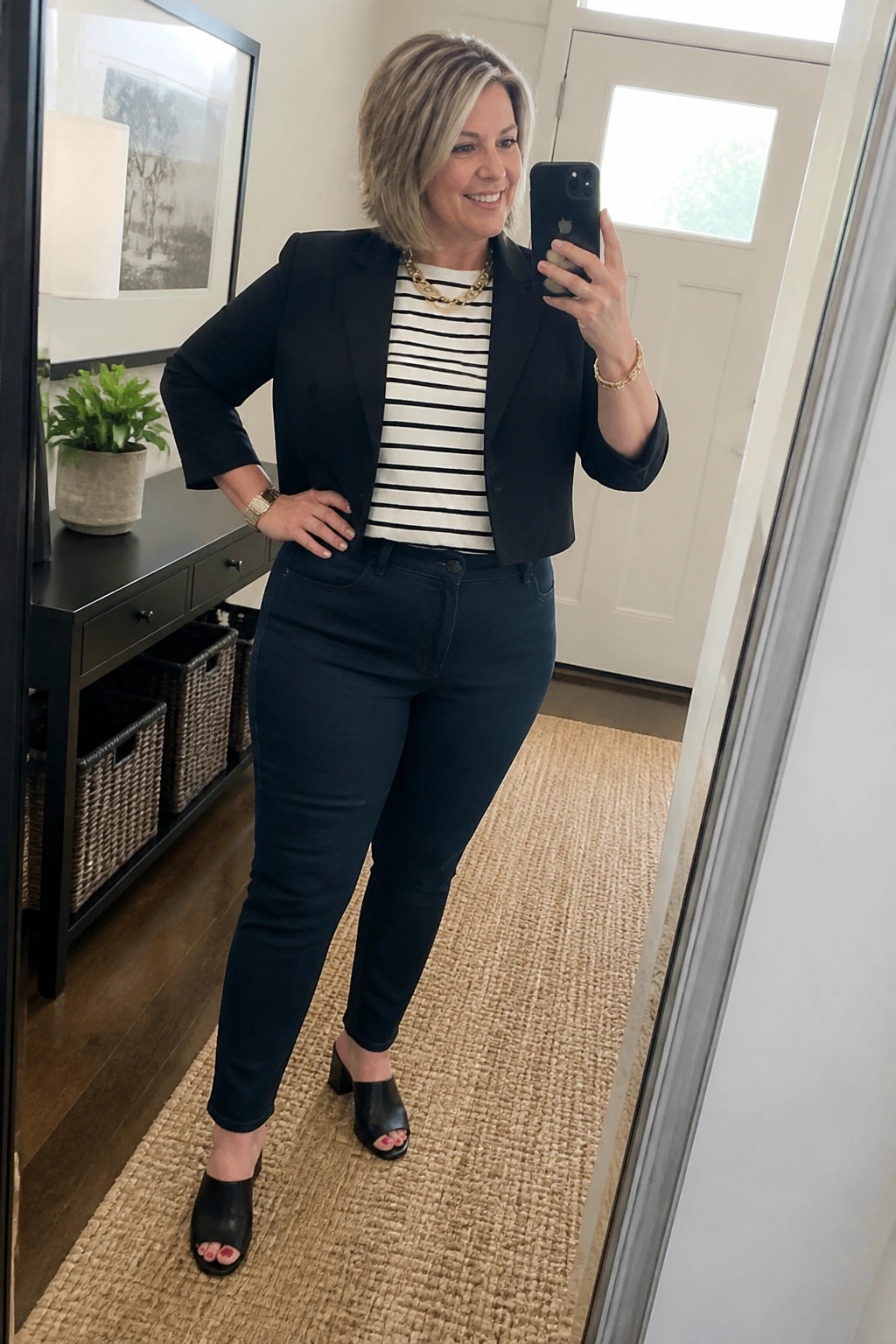 Woman in black cropped blazer over striped top taking mirror selfie with phone