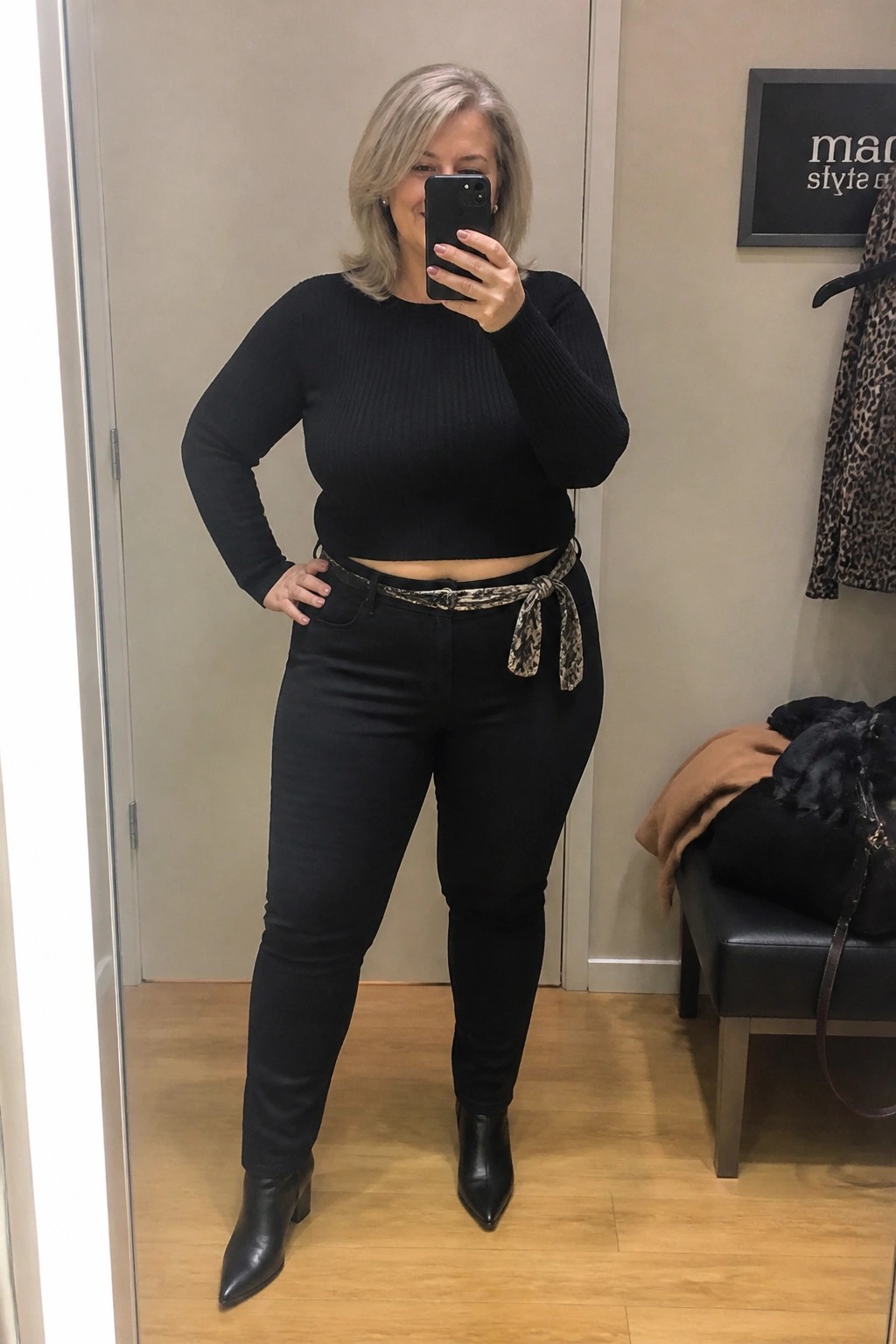 Woman in black crop sweater and jeans with snakeskin belt taking mirror selfie